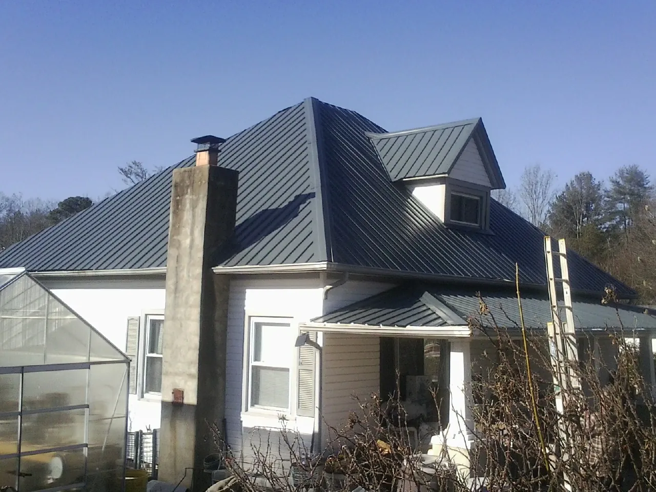 Dark blue standing seam metal roof on a white farmhouse with dormer — Slate & Tile Roof Repair by Roofing Brothers in Holly Ridge
