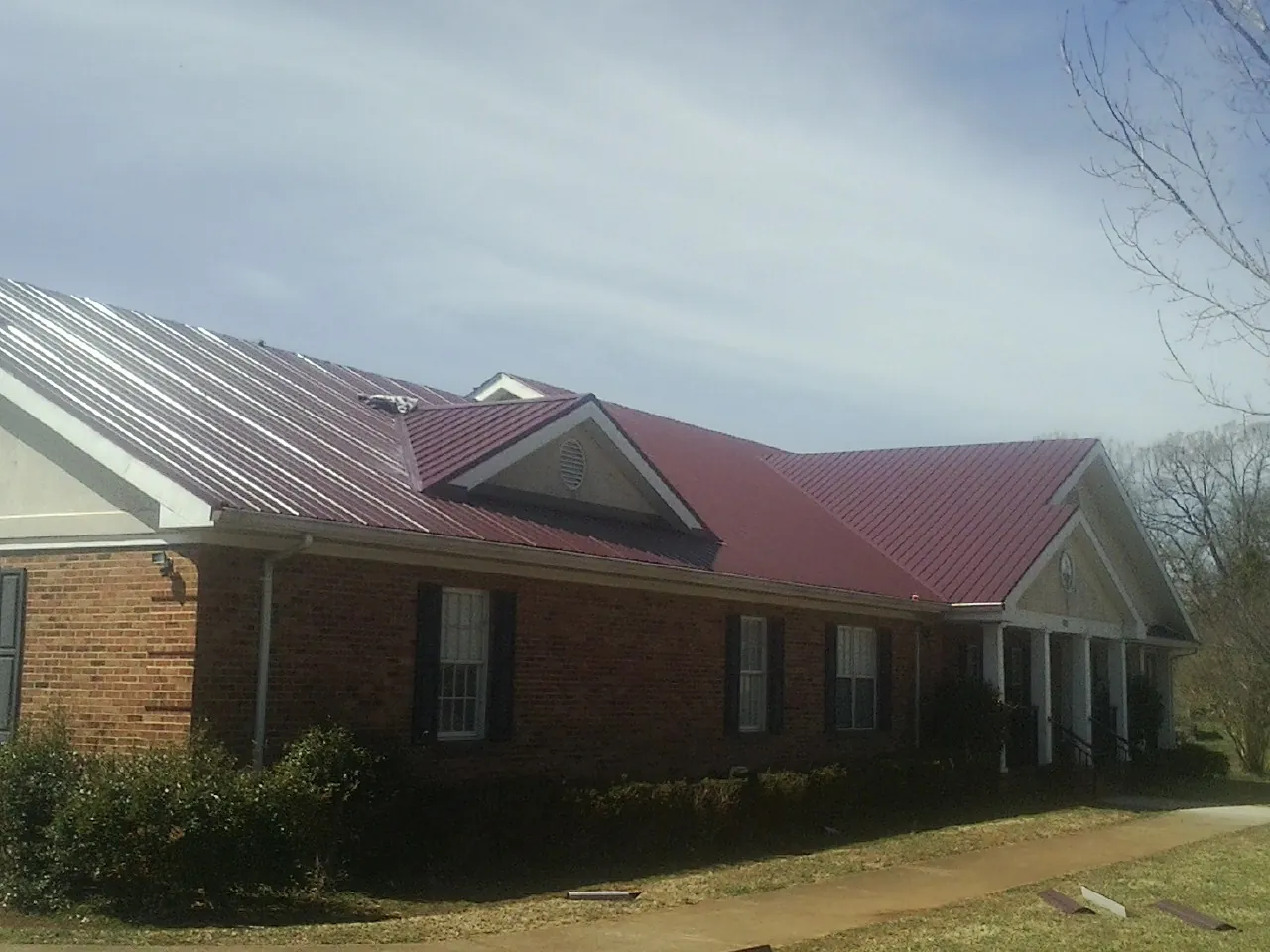 Red metal roof with gabled entries on a long brick building, from a Hail Damage Roof Repair job in Holly Ridge