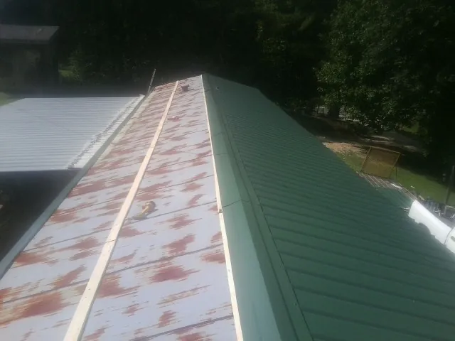 Old rusted panels beside newly installed green metal roofing — Wind Damage Roof Repair by Roofing Brothers in Holly Ridge