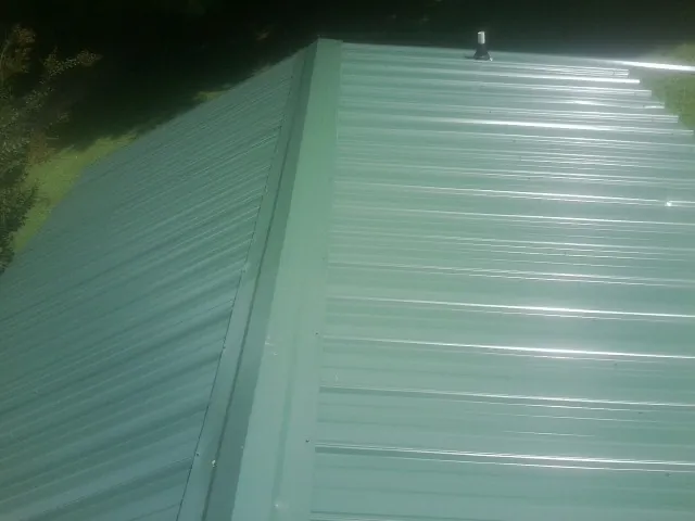 New green metal panels meeting at the ridge of a roof — Flat Roof Repair work by our crew in Holly Ridge