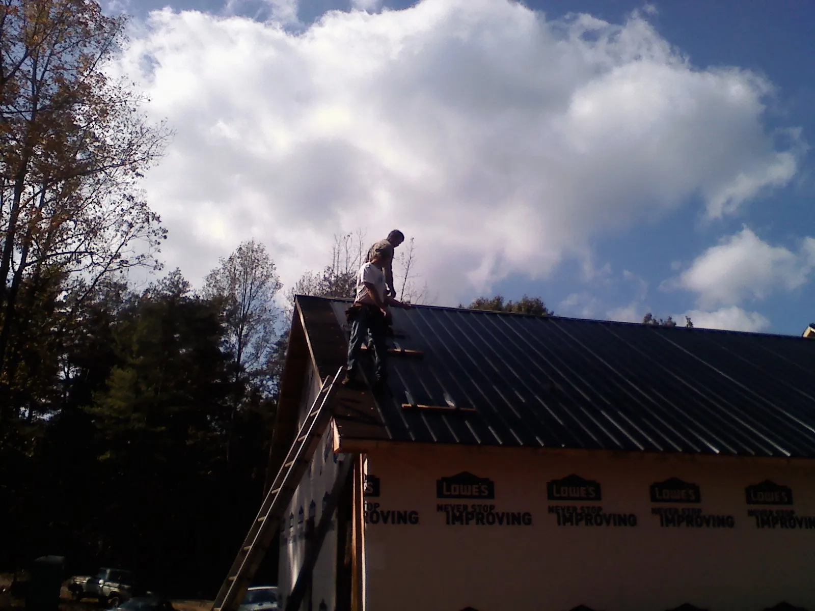 Roofer fastening dark metal panels high against a cloudy sky, from a Roof Inspection job in Holly Ridge