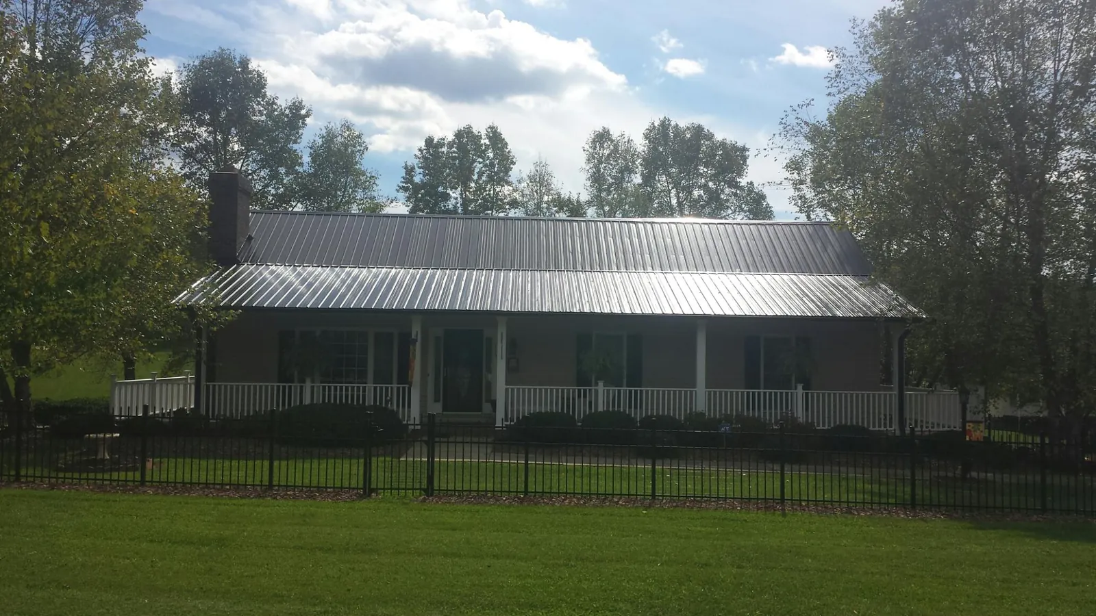 Gray metal roof on a brick ranch with a full width front porch — Gutter Guard Installation work by our crew in Holly Ridge