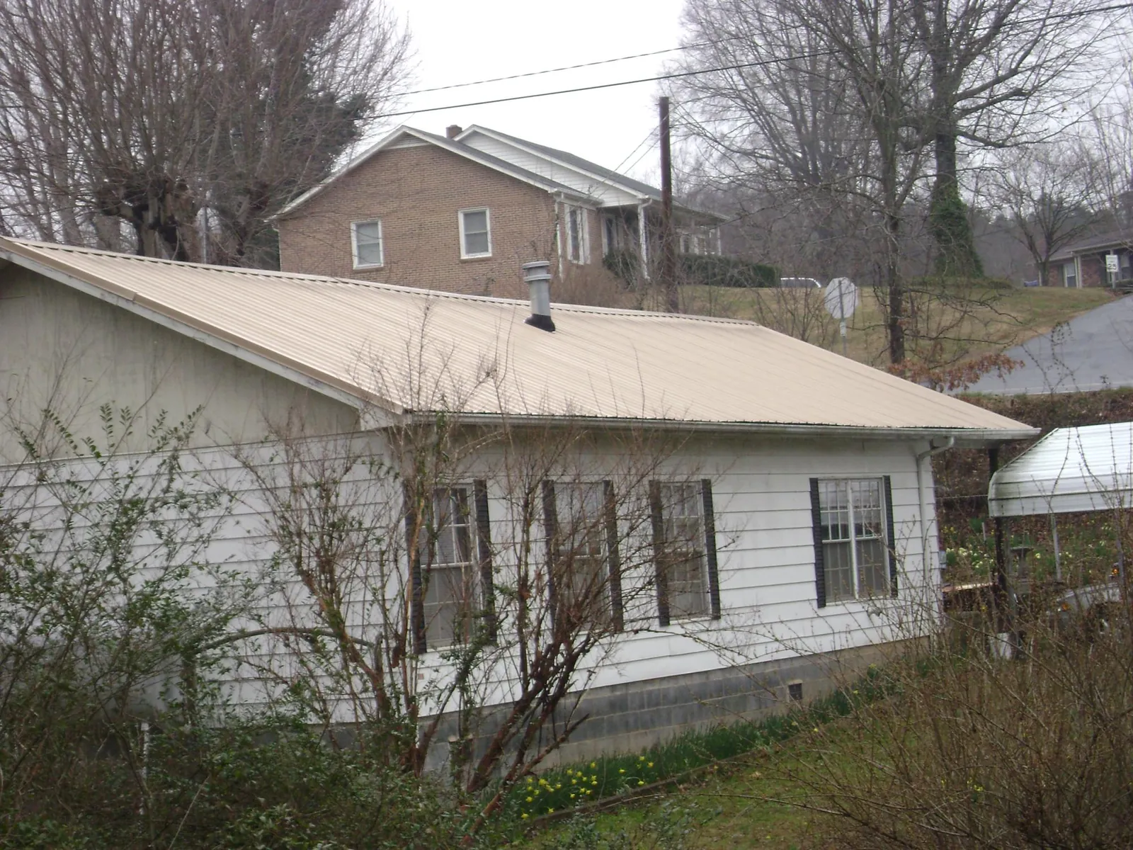 Tan metal roof on a white sided house set into a hillside — Commercial Roofing by Roofing Brothers in Holly Ridge