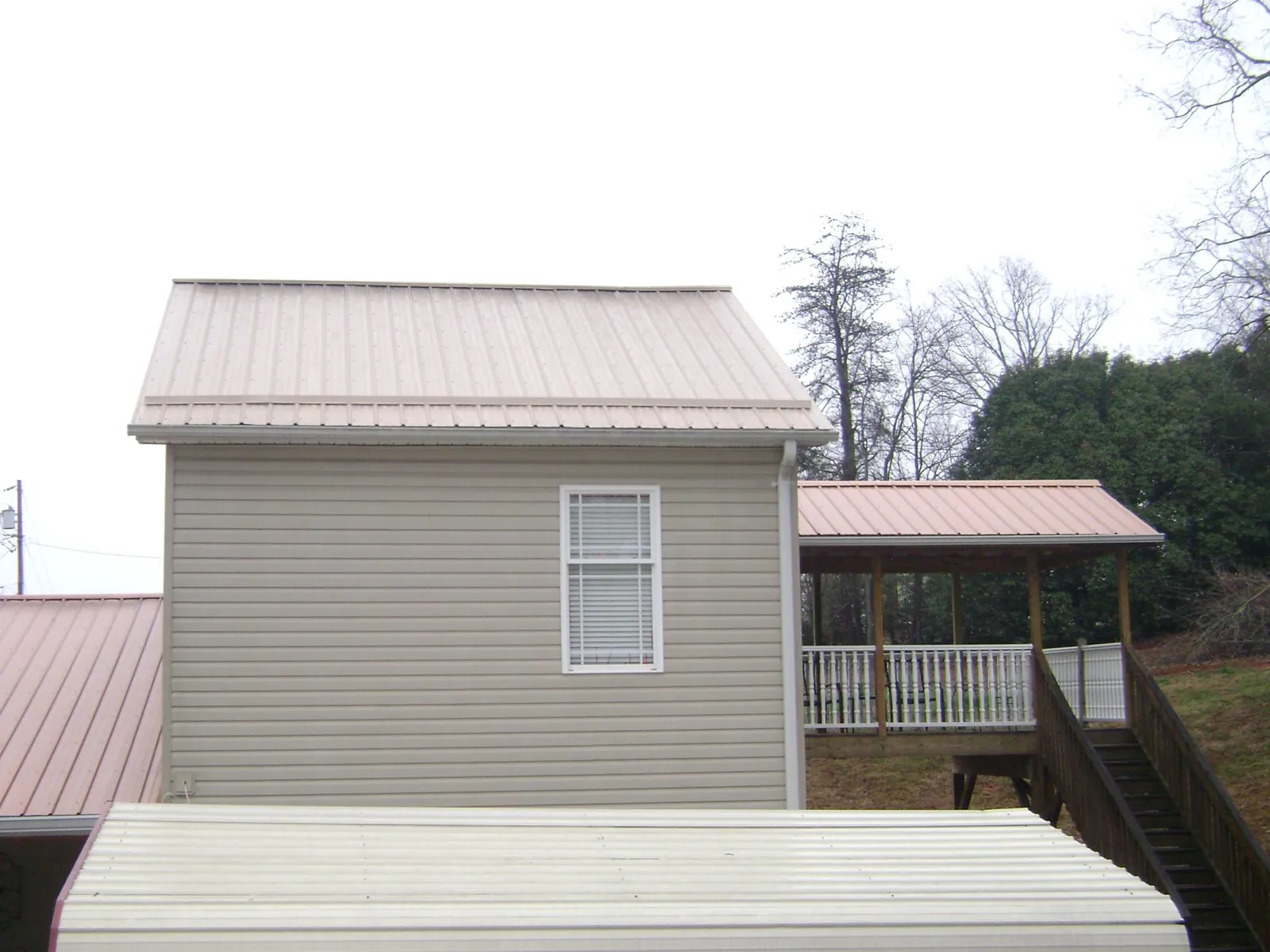 Tan metal roofs on a two story addition and attached porch, from a Roof Replacement job in Holly Ridge