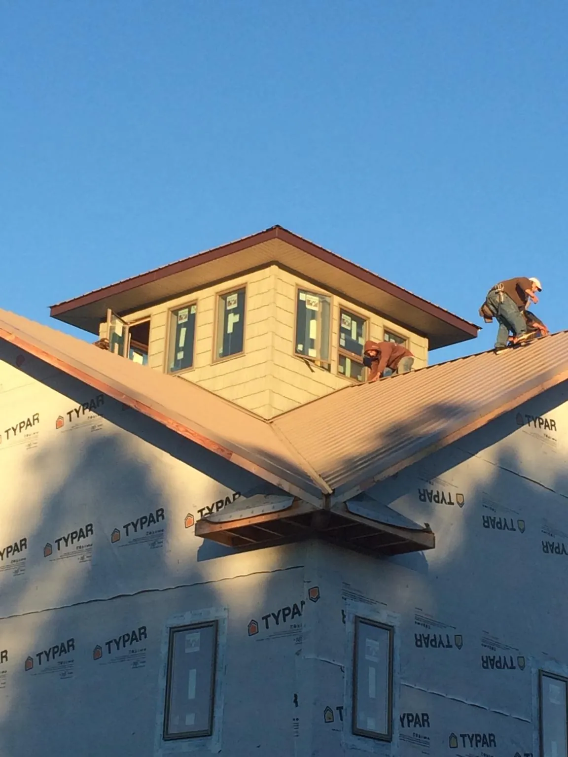Roofers working around a rooftop cupola on a new metal roof at sunset — Roof Waterproofing in Holly Ridge by Roofing Brothers